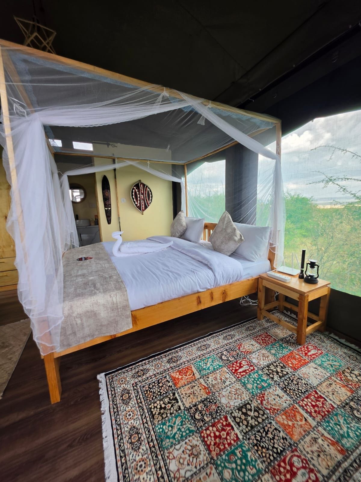 A bed with a canopy, a bedside table with a lamp, and a view of the outdoors.