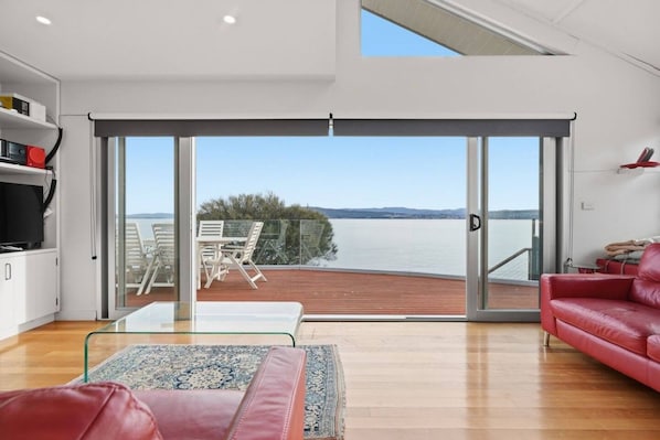 A modern living room with a large sliding glass door leading to a balcony overlooking a body of water.