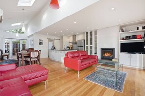 Un amplio salón con un sofá de cuero rojo, una mesa de centro de vidrio y una chimenea.