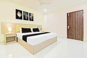 Una habitación de hotel con cama, mesita de noche, lámpara, decoración en la pared y una puerta.