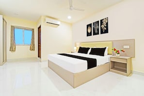 Una habitación de hotel con una cama grande, una mesita de noche con lámpara, un aire acondicionado de pared y una ventana con cortinas.