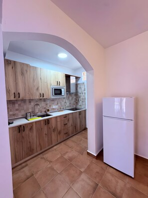 Eine Küche mit Holzschränken, einer Mikrowelle, einem Spülbecken und einem weißen Kühlschrank.