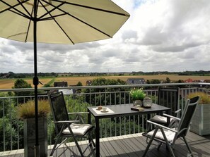A balcony with a table, chairs, and an umbrella. - 47.5.s Waterkant (Wangerland)