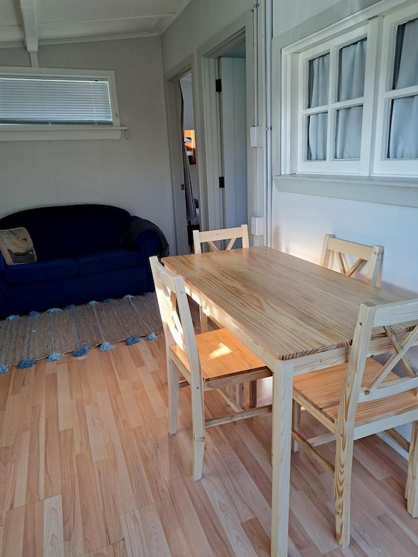 A room with a wooden dining table and chairs, a blue sofa, and a window with curtains.