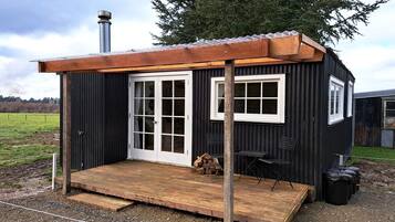 A small, single-story building with a wooden deck, a chimney, and a door leading to an interior space.