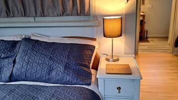 A bedroom with a bed, a nightstand with a lamp, and a door leading to another room.