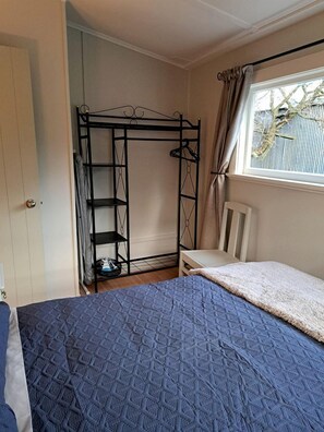 A room with a bunk bed, a metal wardrobe, a chair, and a window with curtains.