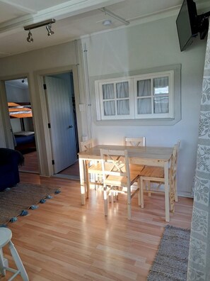 A dining area with a wooden table and chairs, a window with curtains, and a door leading to another room.