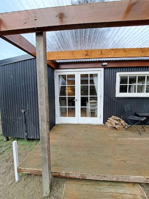 A covered outdoor area with a wooden deck, a sliding glass door leading to an interior space, and a metal chair.