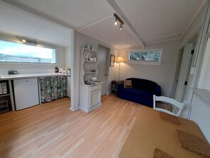 En kompakt opholdsstue med tekøkken, spiseplads og siddeområde.