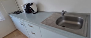 Eine Küche mit einer Spüle aus Edelstahl, einem Gaskochfeld und einer Kaffeemaschine auf der Arbeitsplatte.