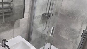 Ett modernt badrum med en dusch som är avskärmad med glasväggar, ett vitt handfat och en spegel ovanför tvättstället.