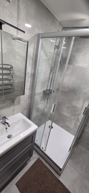 Ein modernes Badezimmer mit einer gläsernen Duschkabine, einem weißen Waschbecken und einem Spiegel über dem Waschtisch.