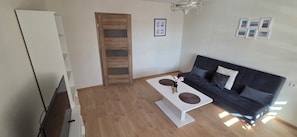 Ein Wohnzimmer mit einem dunkelgrauen Sofa, einem weißen Couchtisch und einer Holztür.