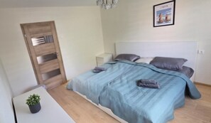 Ein modernes Schlafzimmer mit Bett, Nachttischen, einem kleinen Topf mit Pflanze und einem gerahmten Bild an der Wand.