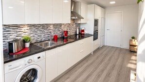 Una cocina moderna con armarios blancos, un tostador de acero inoxidable, una tetera roja y una lavadora integrada.