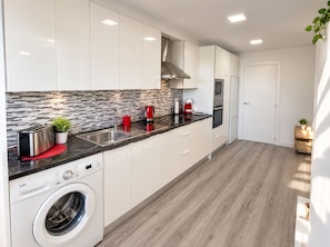 A modern kitchen with white cabinets, a stainless steel toaster, a red kettle, and a built-in washing machine. - Vrbo Property (Costa Adeje)
