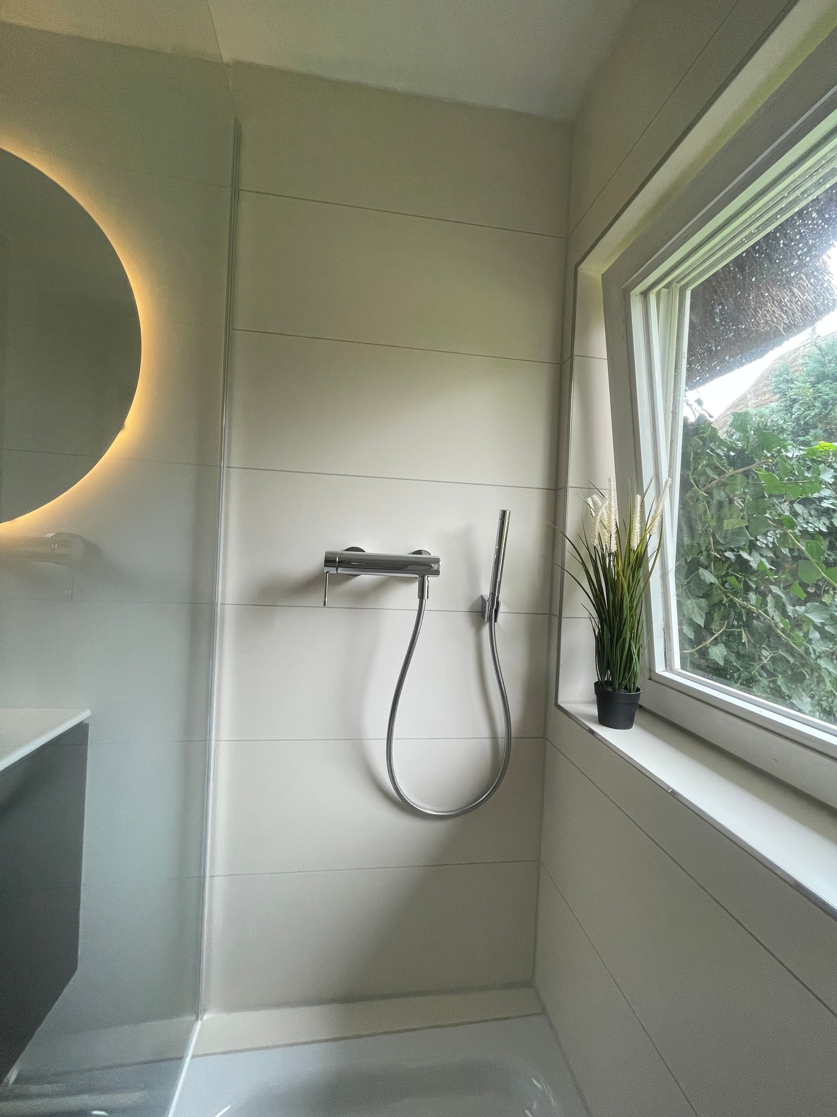 A bathroom with a shower, a sink, and a window with a view of greenery.