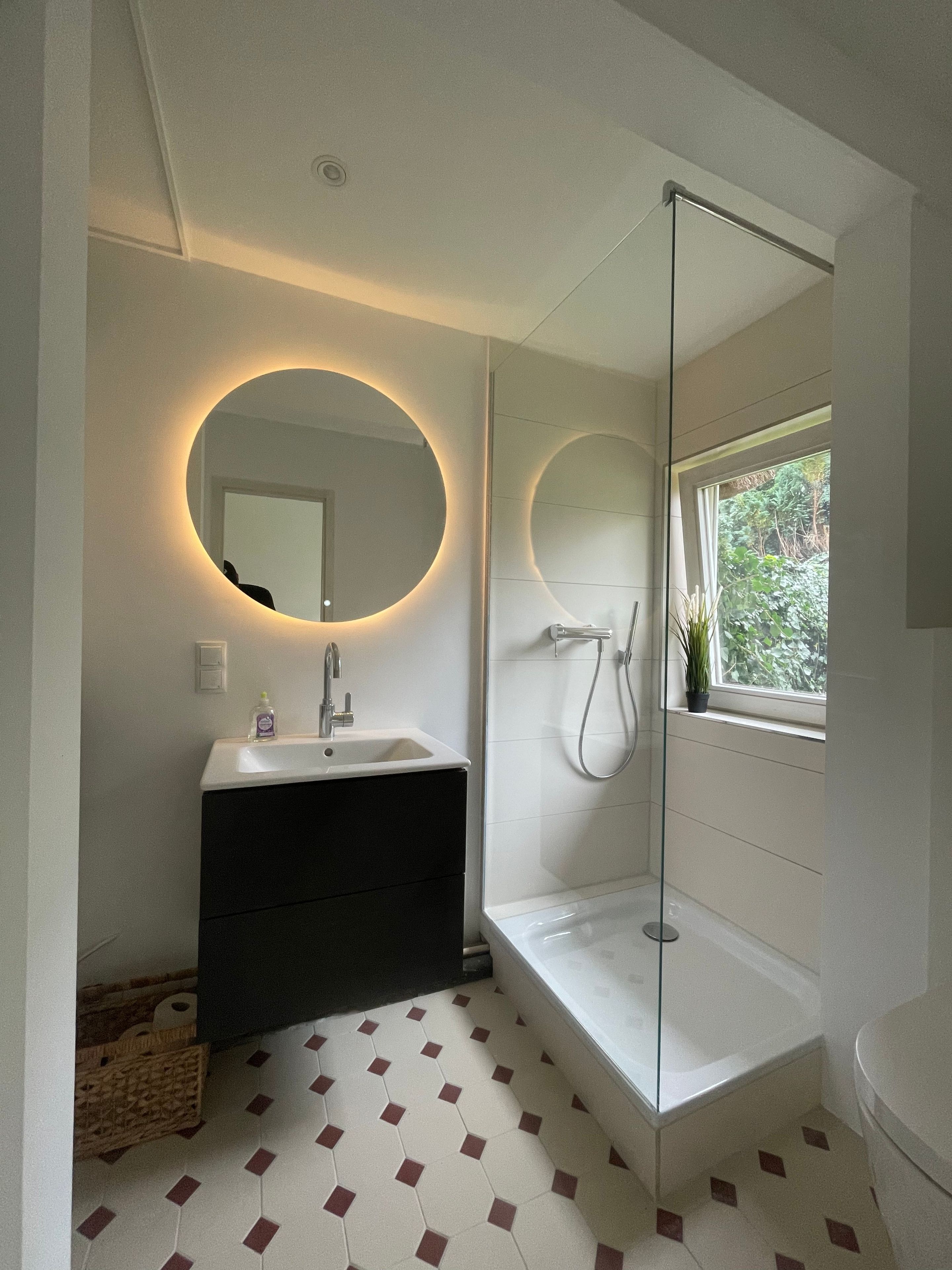 A modern bathroom with a round mirror, a sink, a shower, and a toilet.