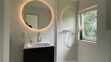 A modern bathroom with a round mirror, a sink, a shower, and a toilet.