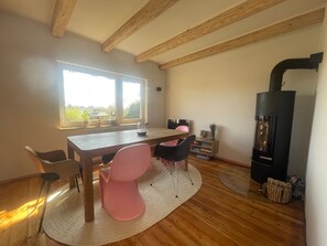 A room with a wooden table, chairs, a fireplace, and a large window. - Cottage under Thatch: Shared Terrace, Garden, Wi-Fi, Near Beach, Designer Furnishings (Schashagen)