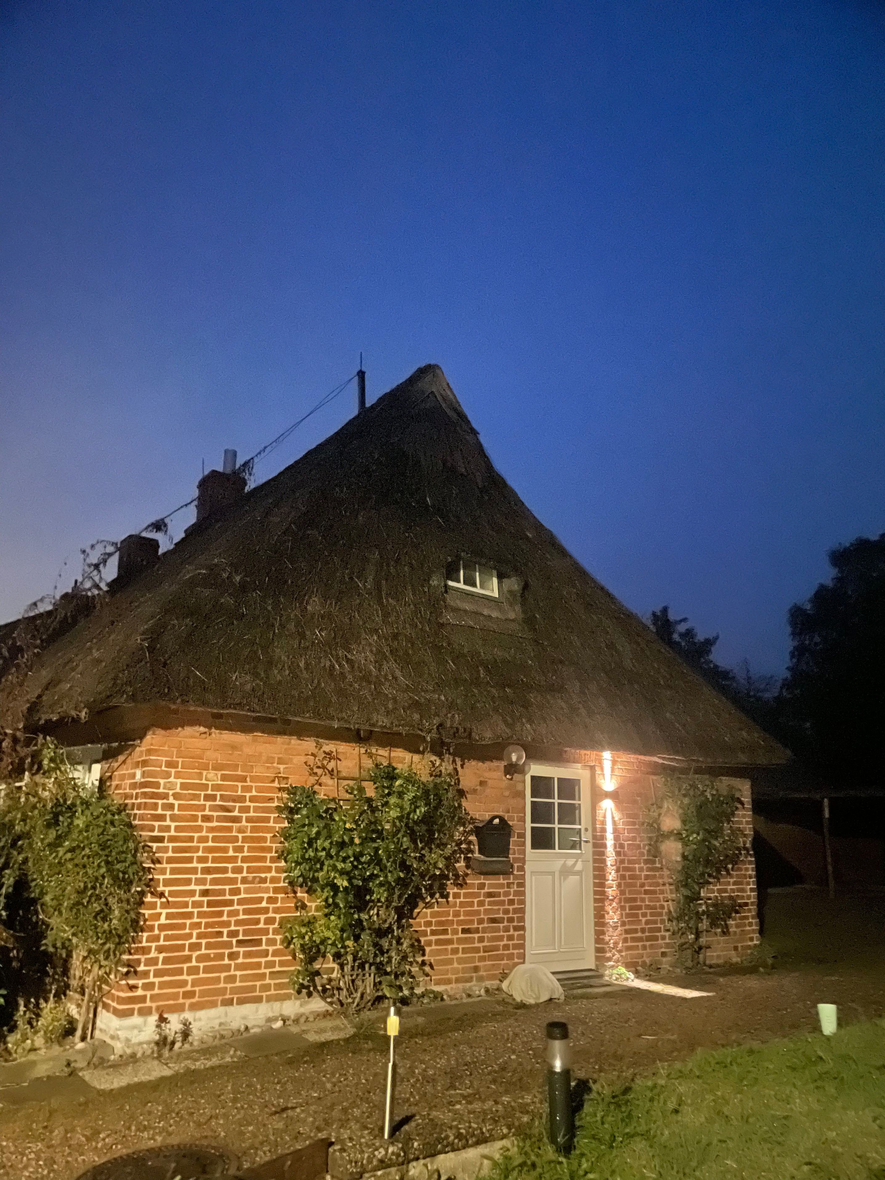 Une maison à toit de chaume, avec une base en briques, une porte blanche et une petite fenêtre.