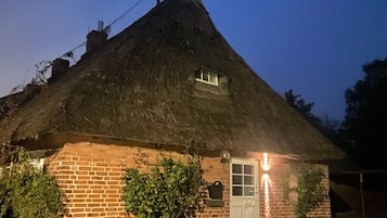 Une maison à toit de chaume, avec une base en briques, une porte blanche et une petite fenêtre.