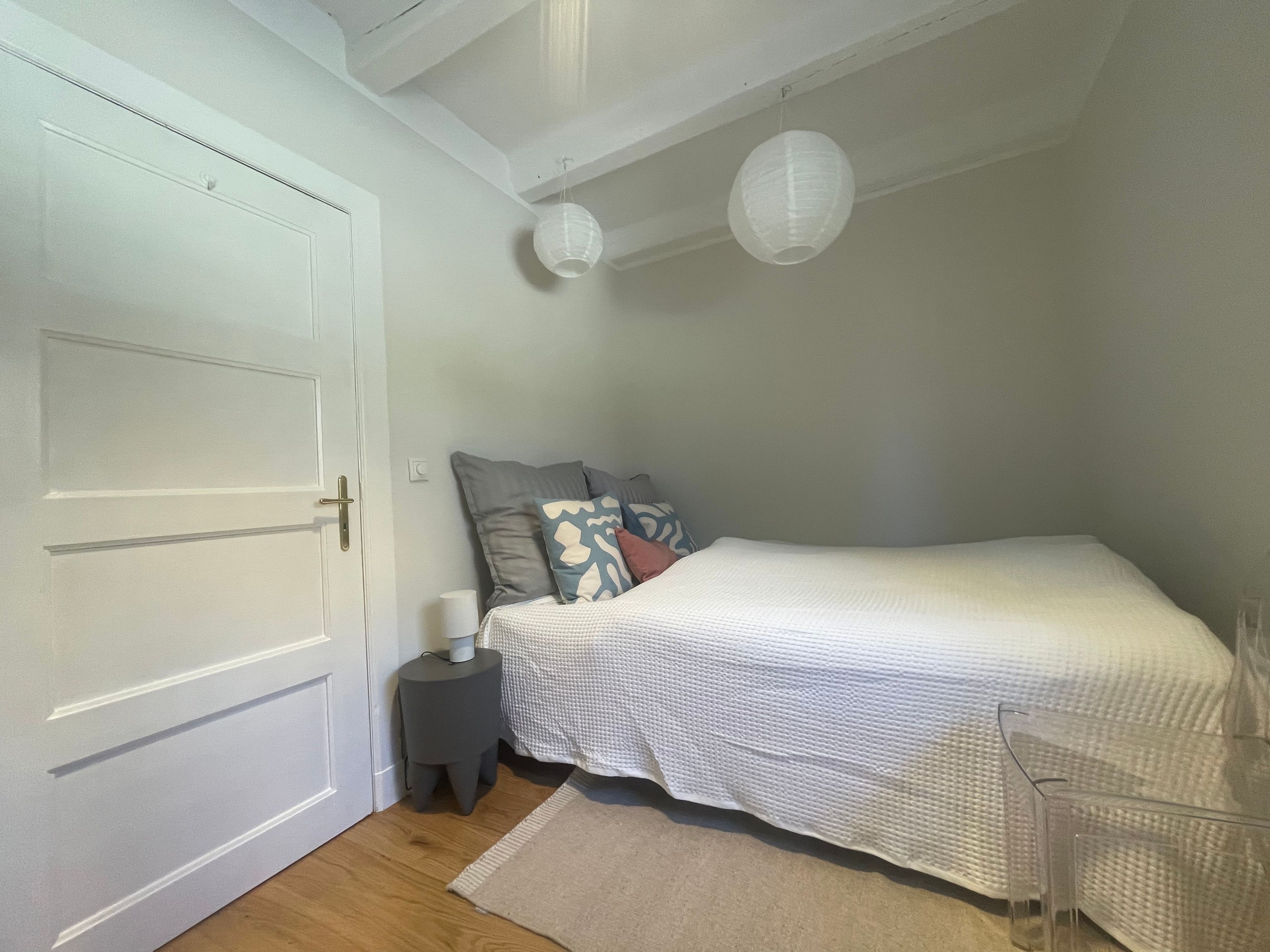 A bedroom with a bed, a bedside table, a lamp, and a door.