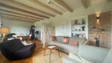 Una sala de estar con sofá, sillón y mesa de centro. Hay una chimenea, una estantería y una lámpara.