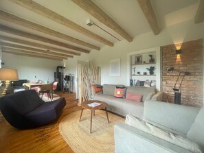A living room with a sofa, armchair, and a coffee table. There is a fireplace, a bookshelf, and a lamp.