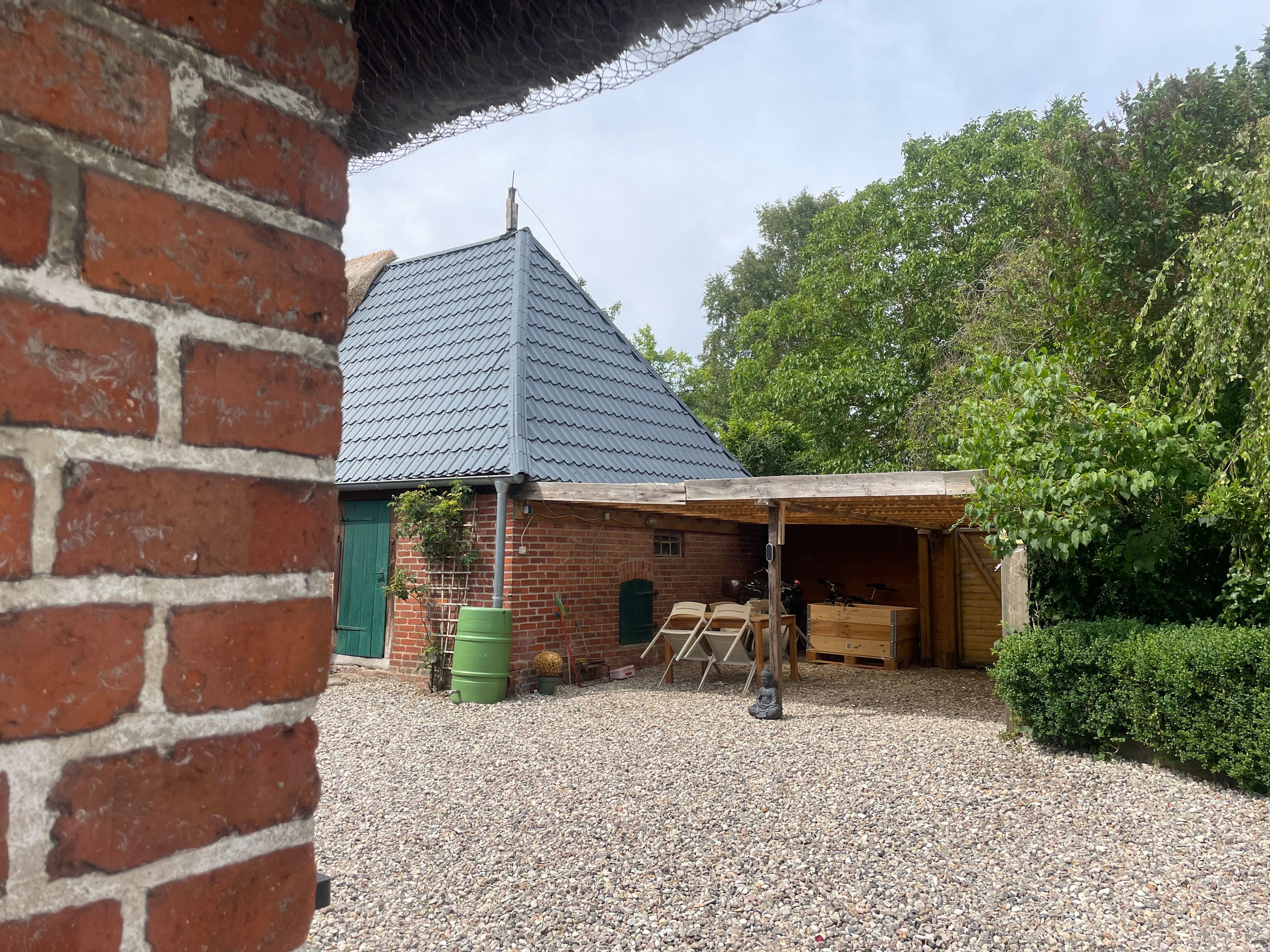A brick building with a sloped roof, a covered outdoor area with a wooden bench, and a gravel ground.