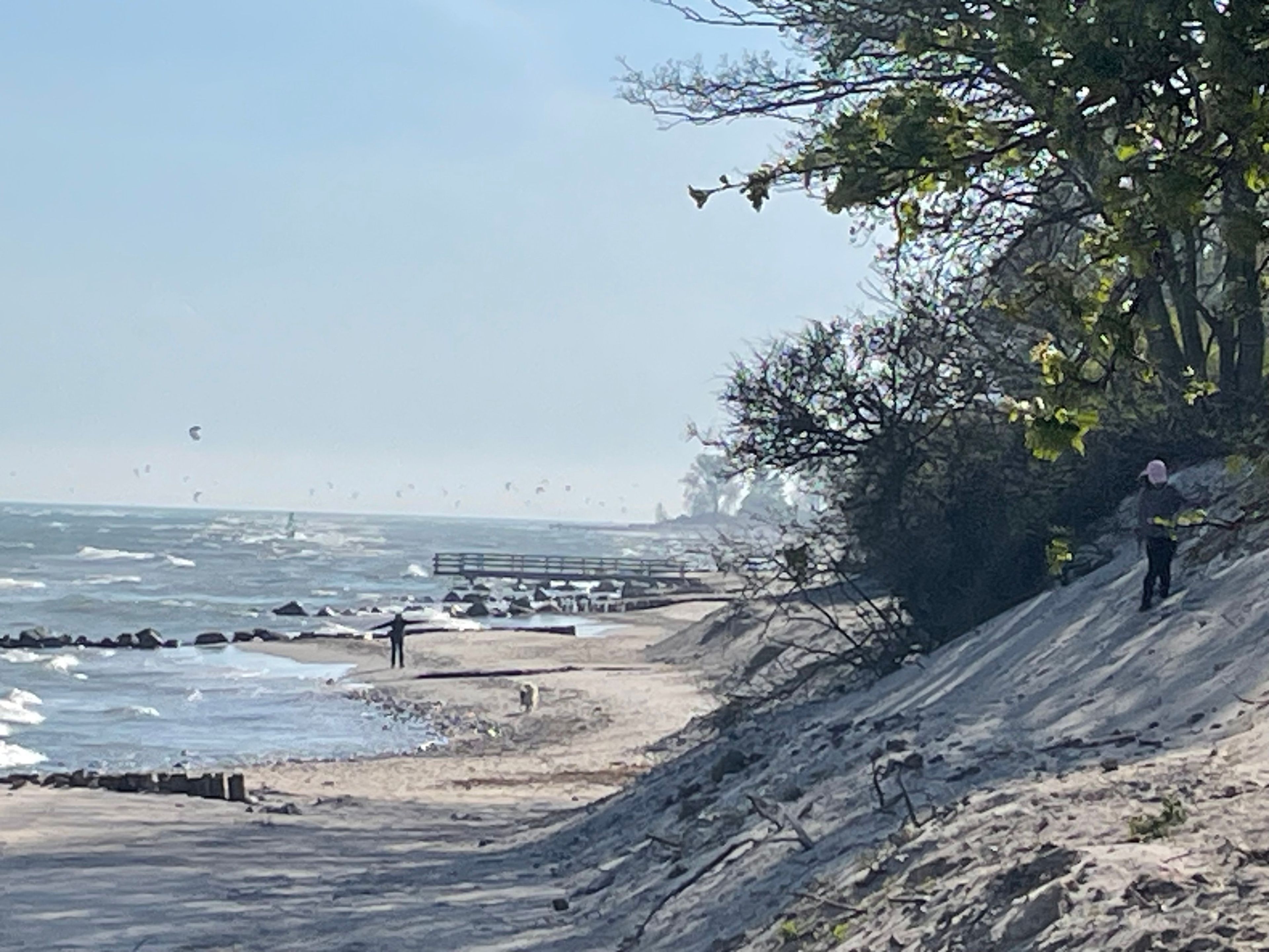 A coastal path with a rocky terrain, a wooden pier, and a person standing on a cliff overlooking the sea.