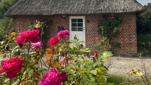 Ein reetgedecktes Cottage mit Ziegelaußenwand, einer weißen Tür und einem kleinen Fenster.