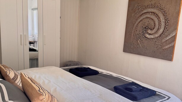 Un dormitorio con cama, armario, un cuadro y ventana.
