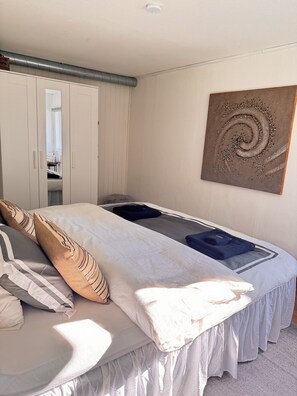 A bedroom with a bed, a wardrobe, a painting, and a window.