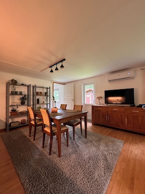 A dining area with a wooden table and chairs, a kitchen with a TV, and a living area with a fireplace.