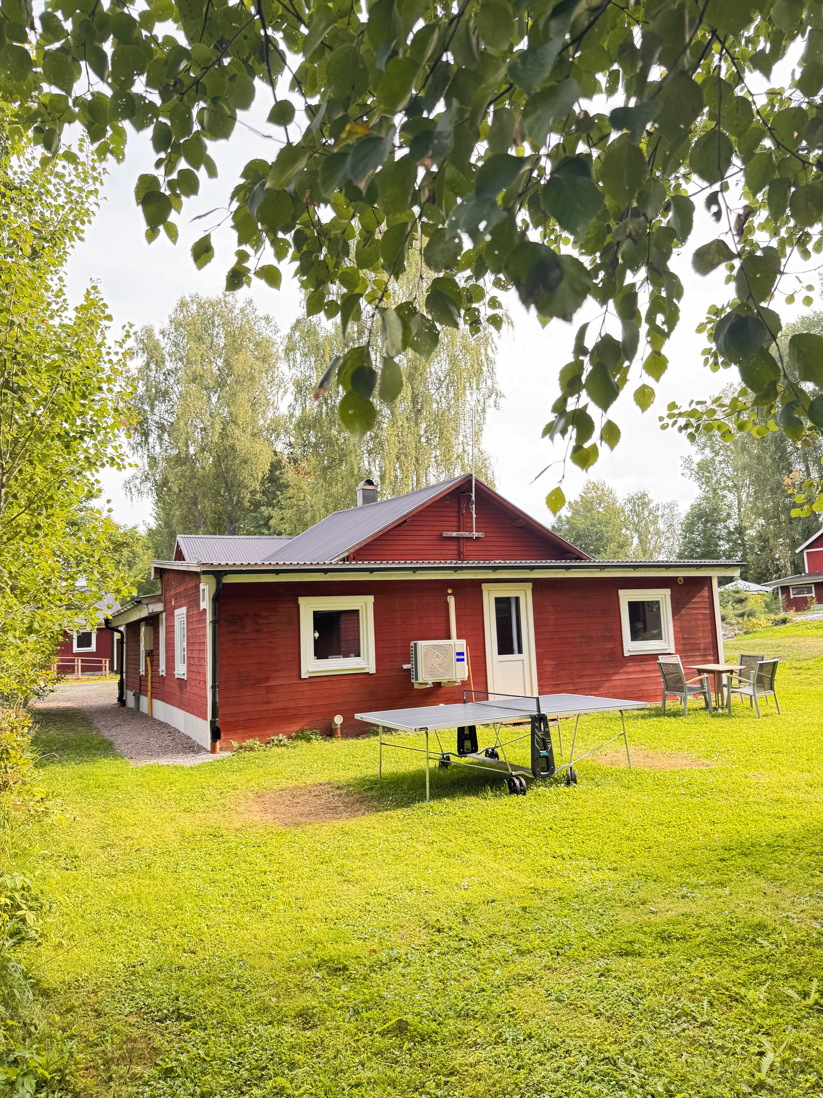 Ett rött hus med en takförsedd uteplats, ett bord och stolar.