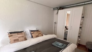 Una cama bien hecha con una colcha blanca y negra, dos almohadas y toallas dobladas.