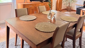 Un comedor con mesa de madera, sillas y televisor al fondo.
