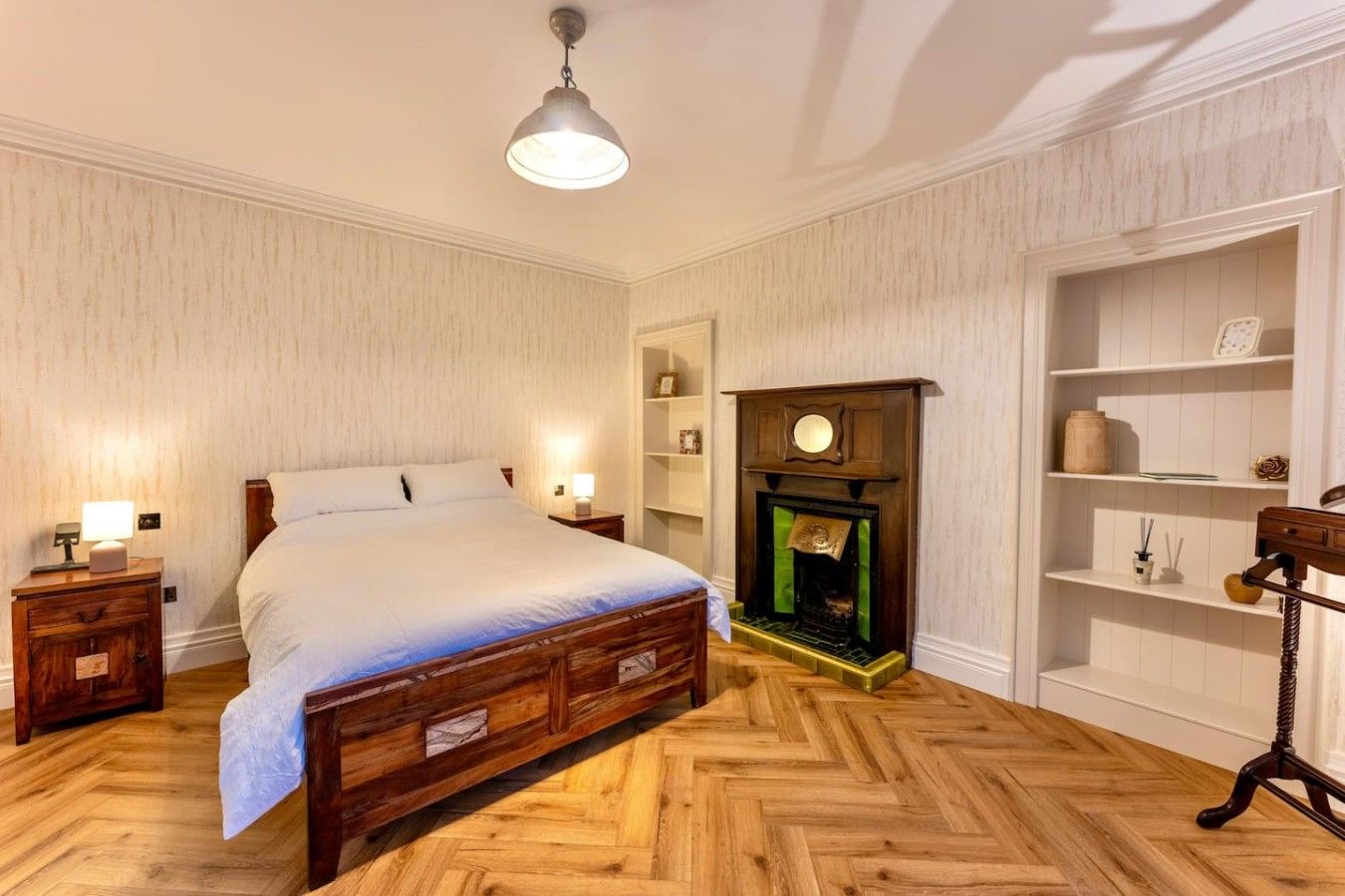A bedroom with a wooden bed, bedside tables, a fireplace, and a shelf with decorative items.