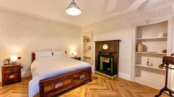 A bedroom with a wooden bed, bedside tables, a fireplace, and a shelf with decorative items.