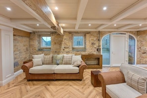 A room with a herringbone-patterned wooden floor, a brown leather sofa with multiple cushions, and a stone wall. - Distillers Louge by Old Carrick Mill (Carrickmacross)