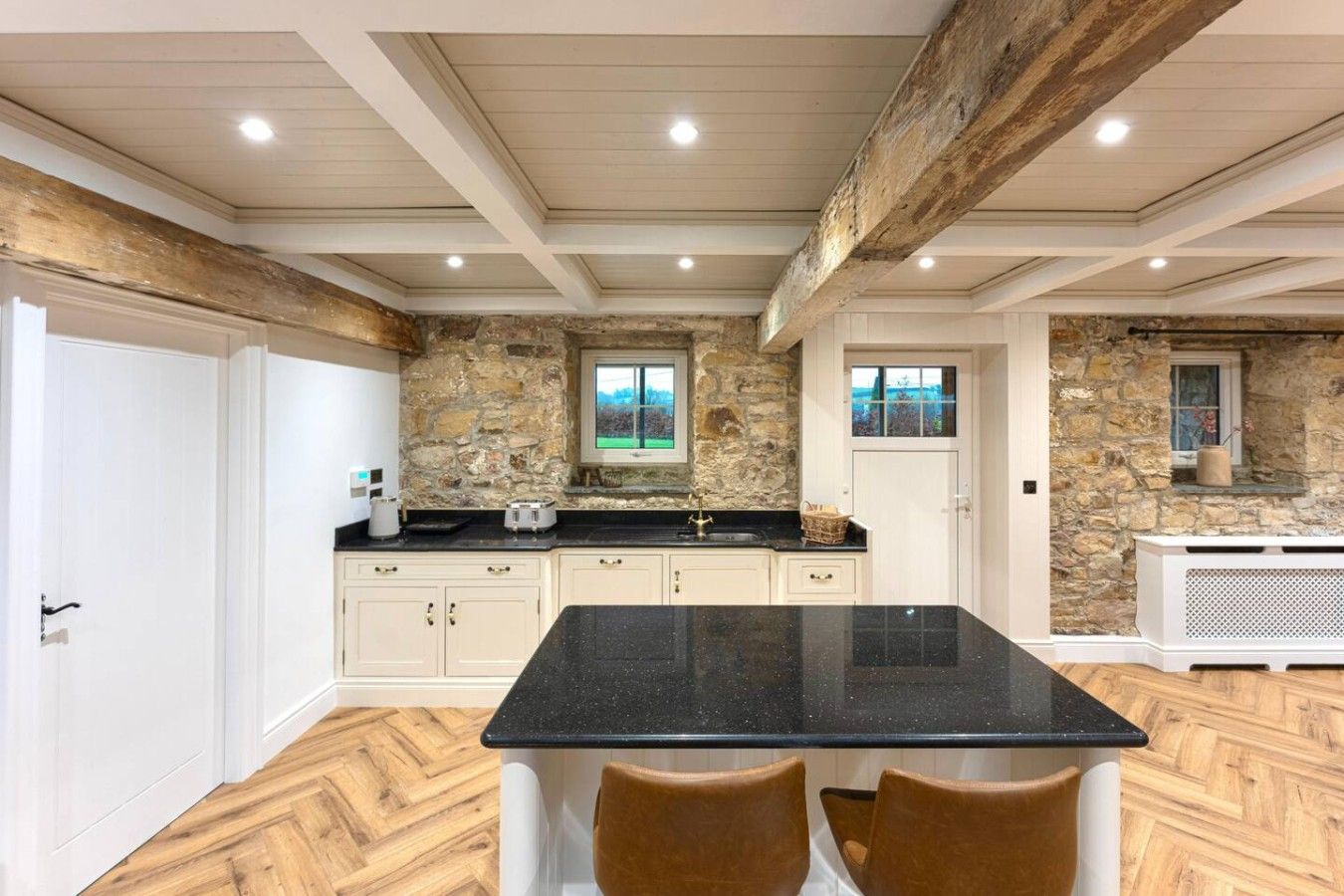 Cocina con pared de piedra, encimera negra y suelo de madera.