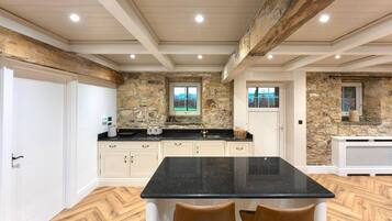 Cocina con pared de piedra, encimera negra y suelo de madera.