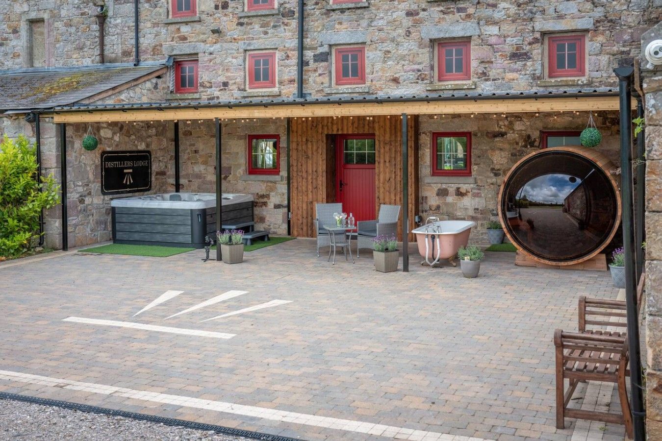 A stone building with a wooden porch, a hot tub, and a large barrel.