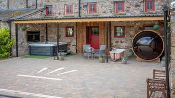 A stone building with a wooden porch, a hot tub, and a large barrel.