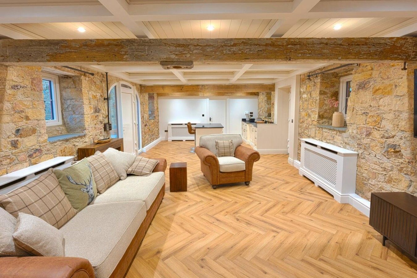 A spacious living area with a herringbone floor, stone walls, a sofa set, and a fireplace.