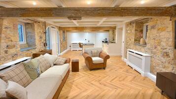 A spacious living area with a herringbone floor, stone walls, a sofa set, and a fireplace.