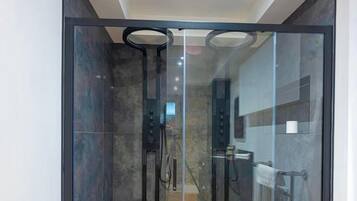 A modern bathroom with a glass shower enclosure, a wooden floor, and a visible shower control panel.