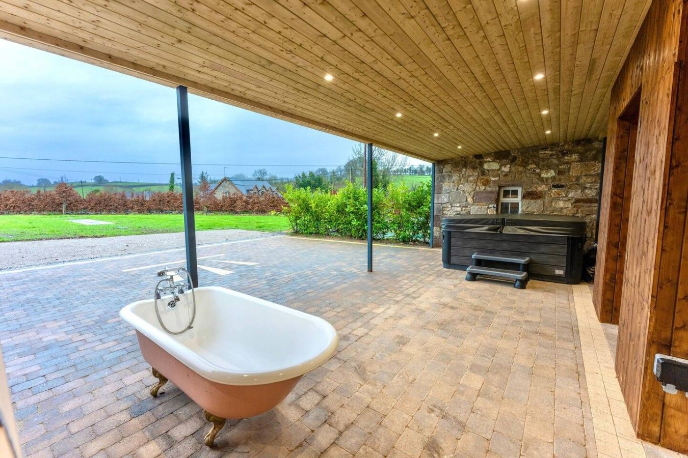 A bathroom with a freestanding bathtub, a stone wall, and a wooden ceiling.